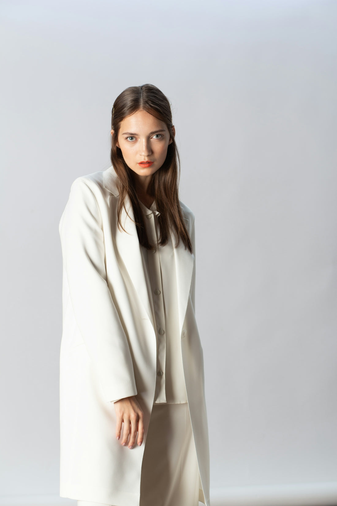 Woman in white coat and pants stands against gray background