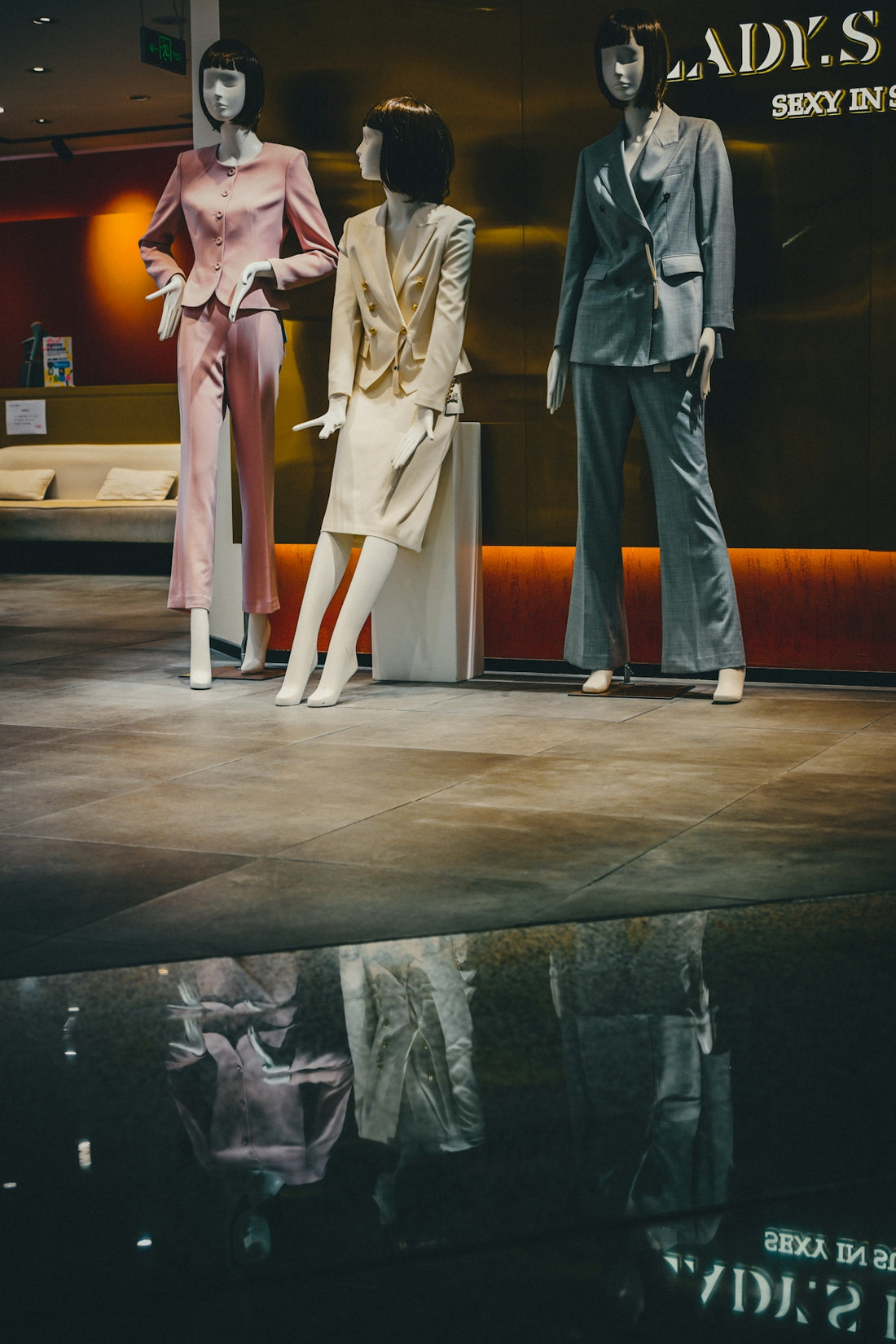 Three mannequins wearing business suits in a store window with a floor reflection