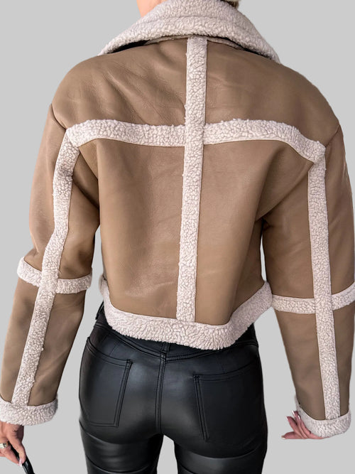 Brown leather jacket with white stitching worn by a person, standing against a neutral background.