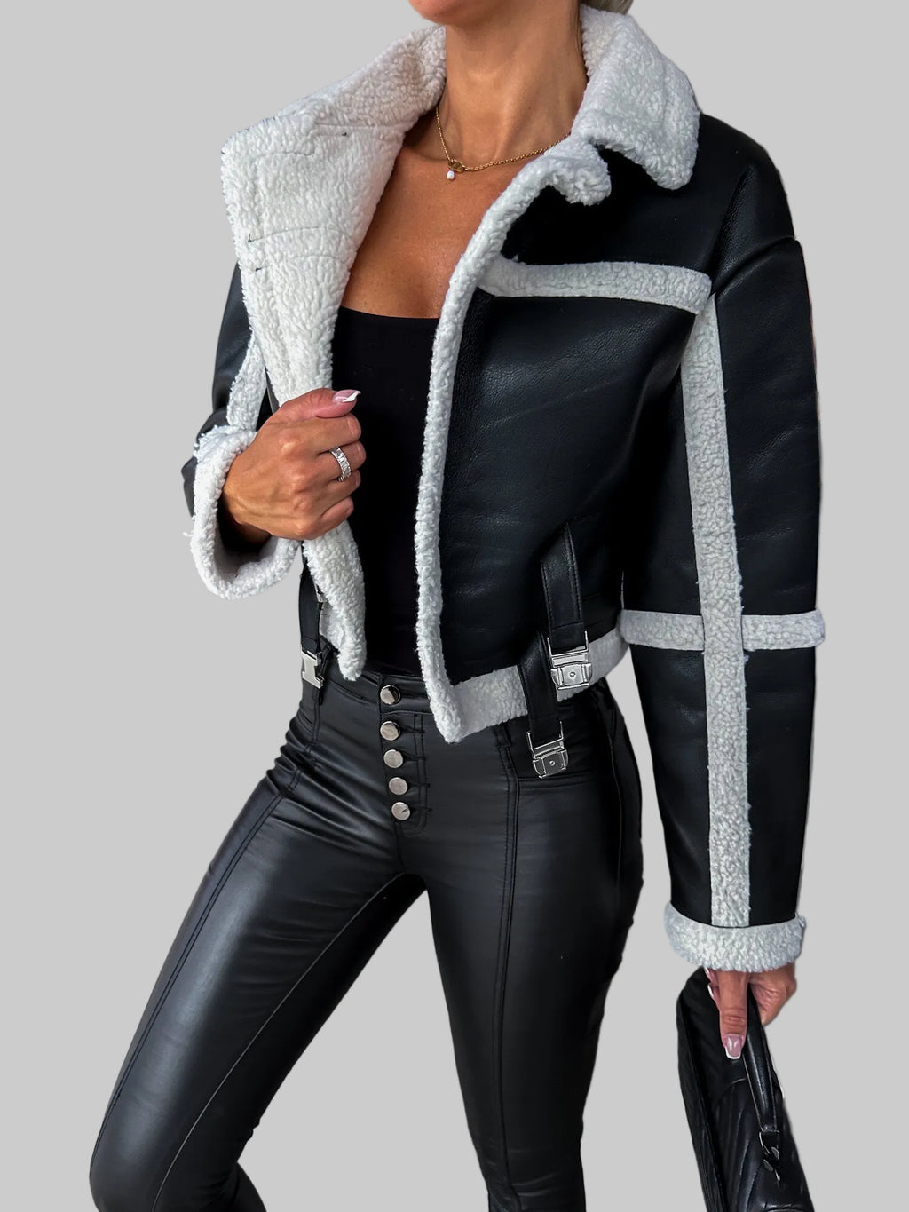 Person wearing a black leather jacket with white fur trim indoors.