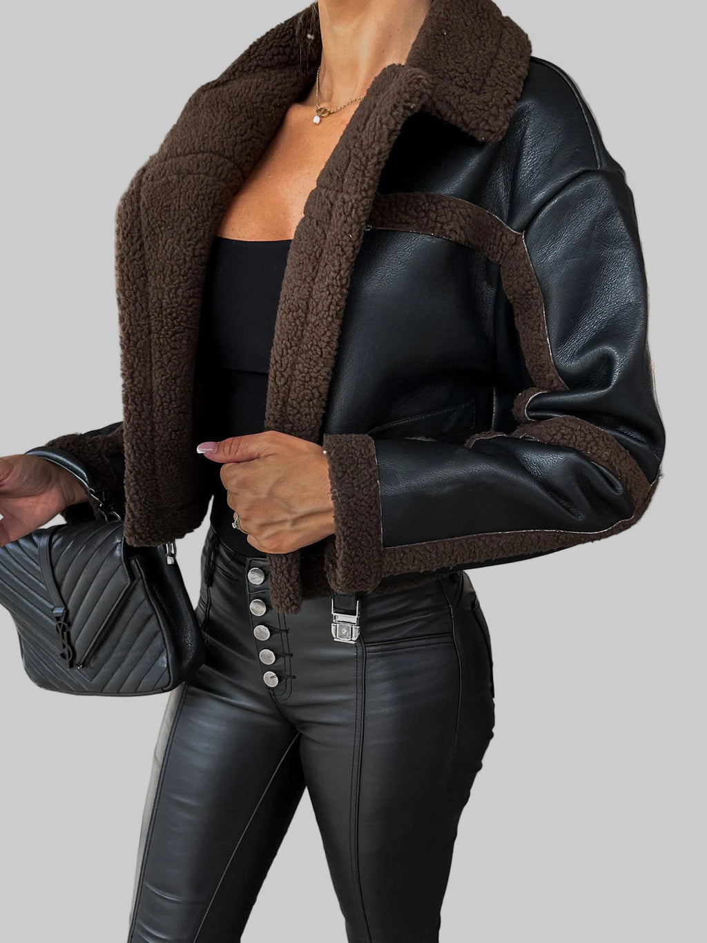 Person wearing a black leather jacket with brown shearling collar in an urban setting