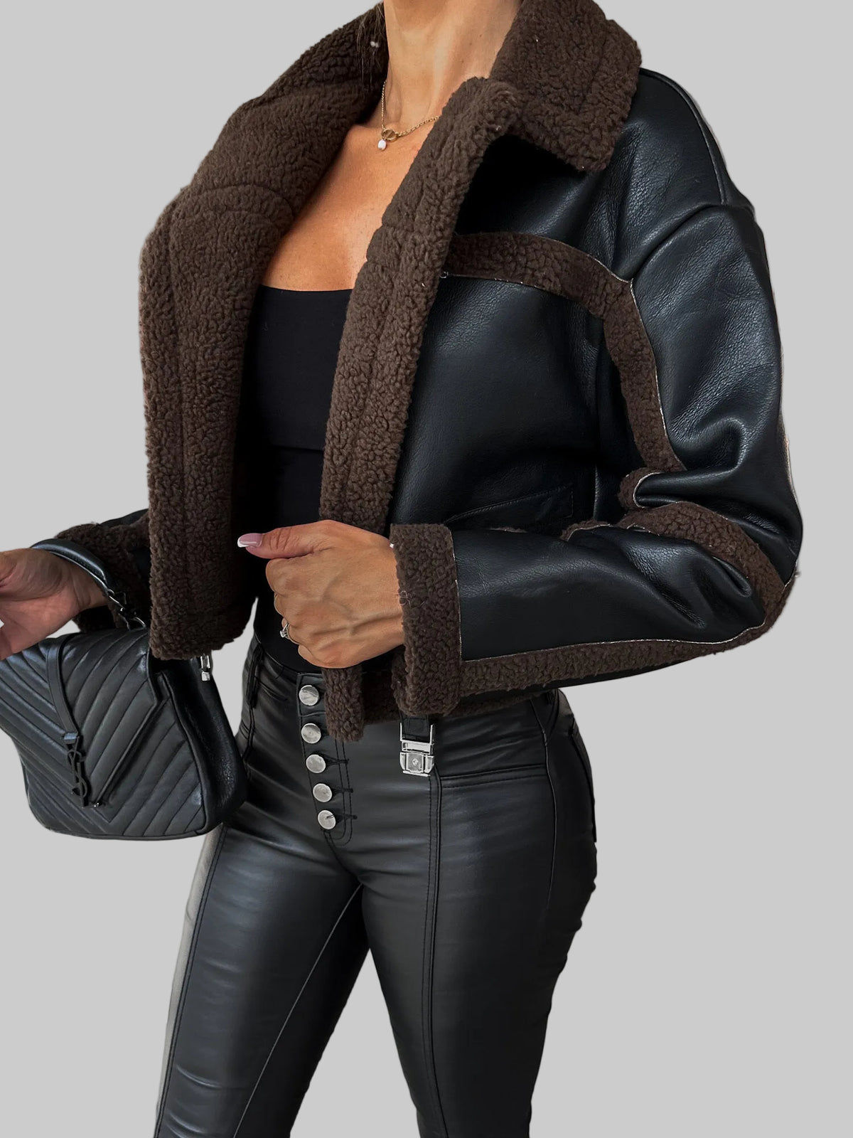 Person wearing a black leather jacket with brown shearling collar in an urban setting