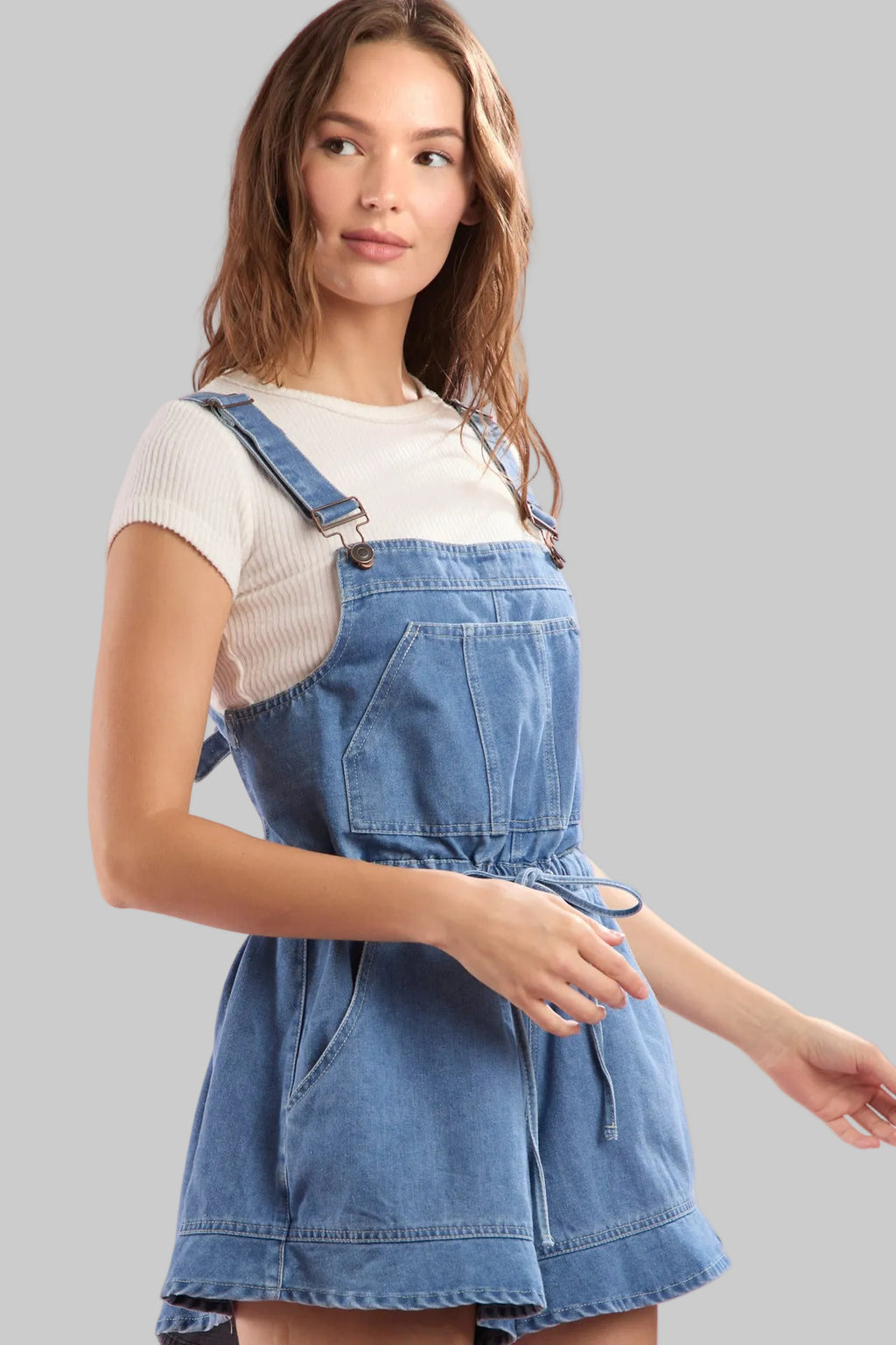 Woman wearing a denim overall dress against a pink background