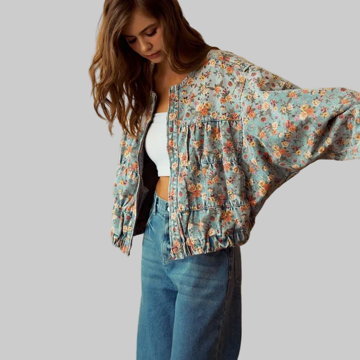 Woman wearing a floral jacket and blue jeans against a beige wall.