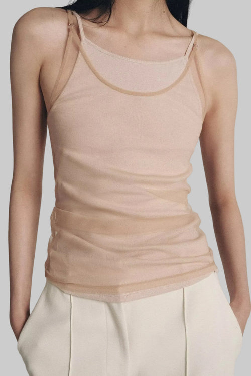 Person wearing a beige tank top and white pants against a neutral background