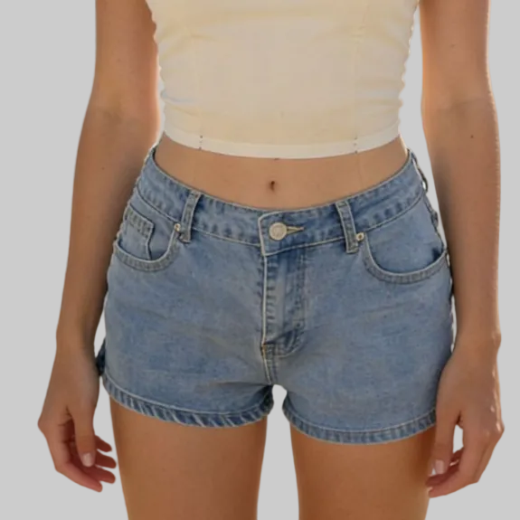 Person wearing a white crop top and blue denim shorts on a beach.