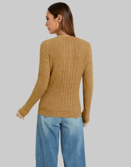 A woman shown from the back wearing a ribbed knit sweater in a warm camel brown color, paired with blue jeans, against a plain light gray studio background.