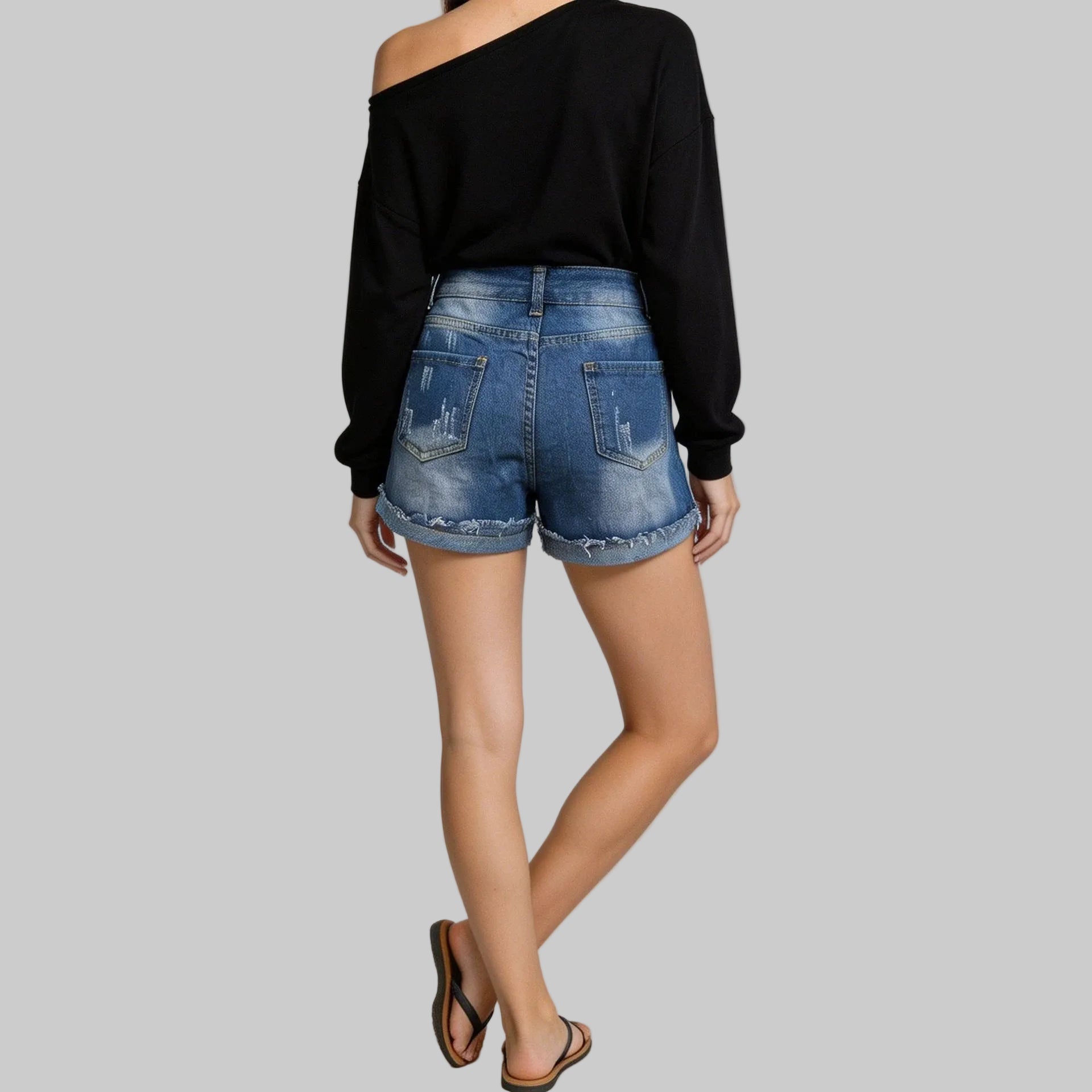 Person wearing a black off-shoulder top and blue denim shorts on a plain background