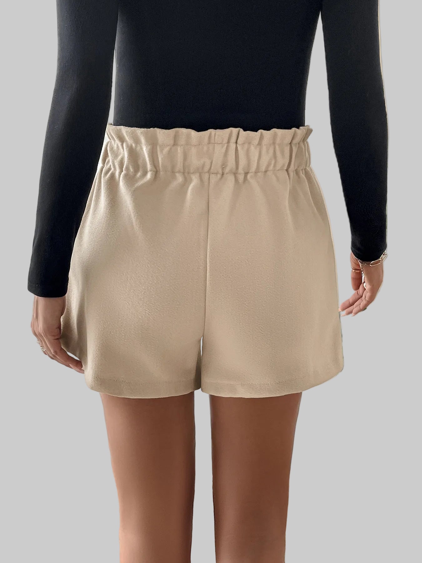 Person wearing beige shorts and a black top in a room with a plant.