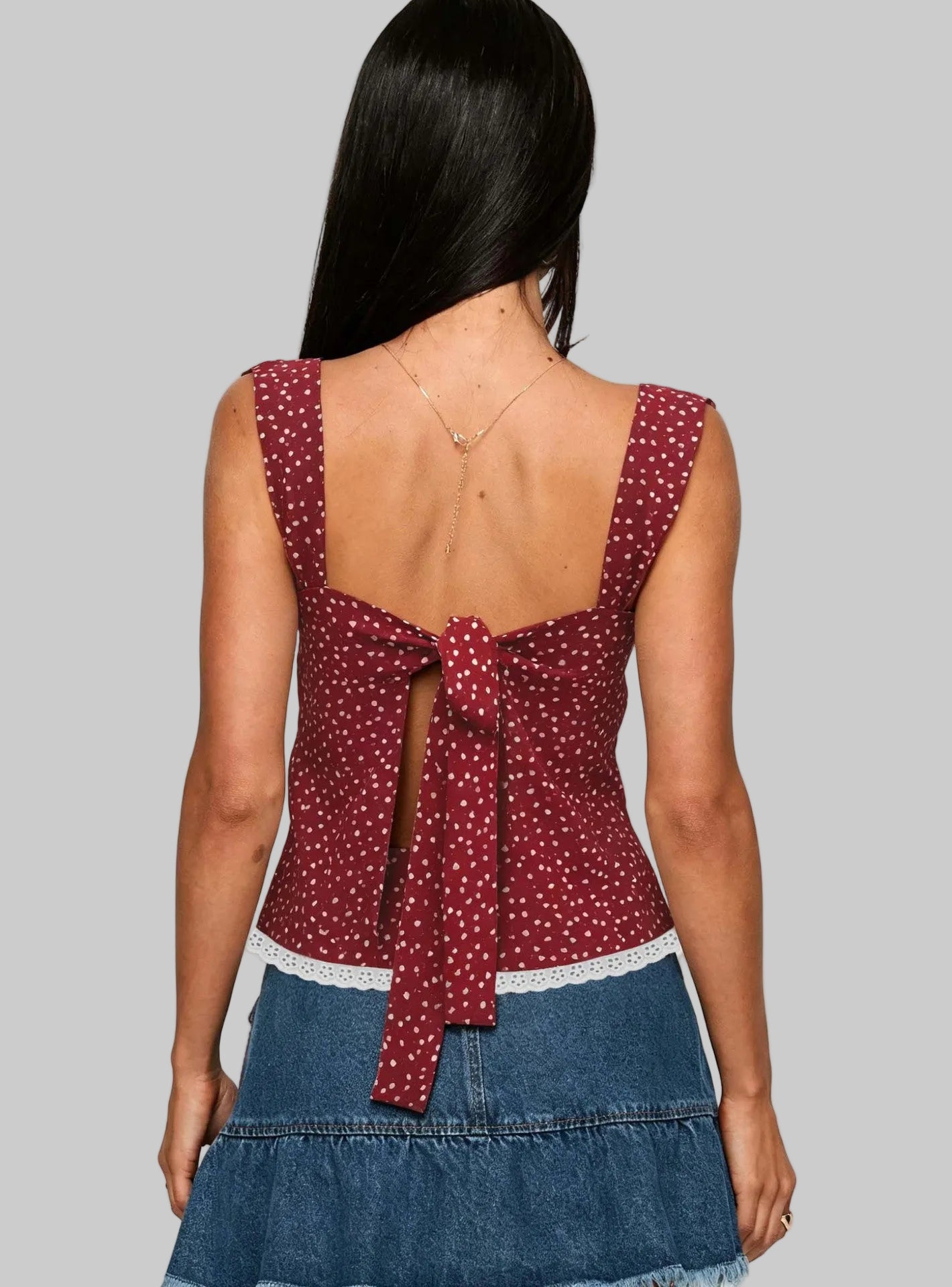 Woman wearing a red polka dot top with an open back and denim skirt on a white background