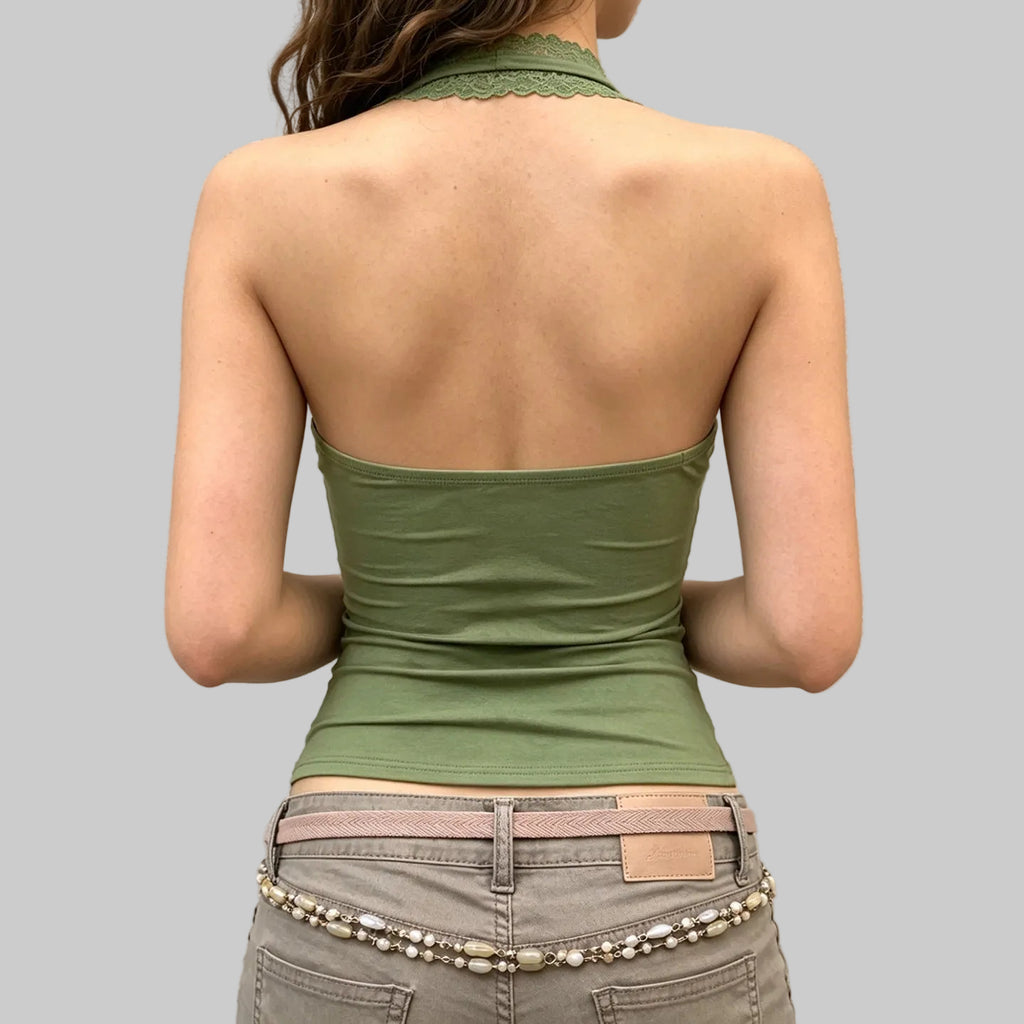 Person wearing a green halter top and beige pants against a light gray wall.