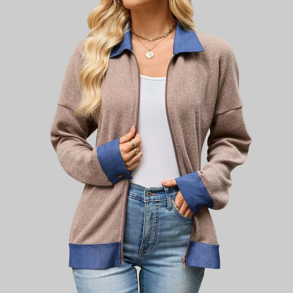 A woman wearing a taupe-brown zip-up cardigan with contrasting blue collar, cuffs, and hem, styled over a white tank top and blue jeans against a plain white background.
