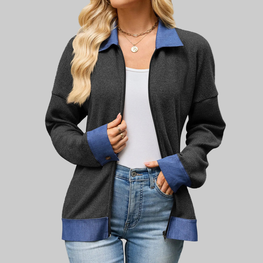 A woman wearing a dark charcoal gray zip-up cardigan with contrasting blue collar, cuffs, and hem, styled over a white tank top and blue jeans.
