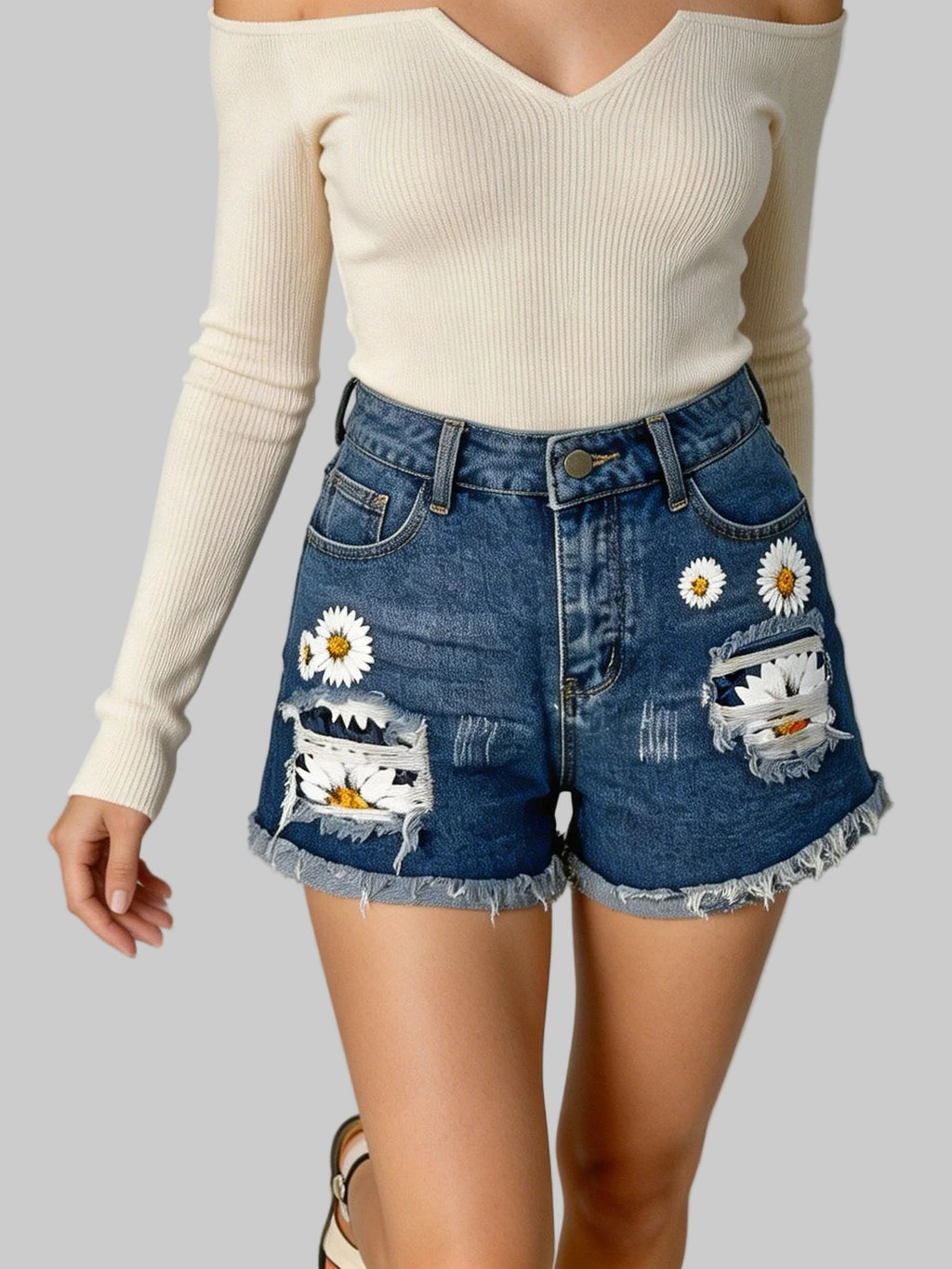 Person wearing a cream long-sleeve top and denim shorts with floral patches on a gray background