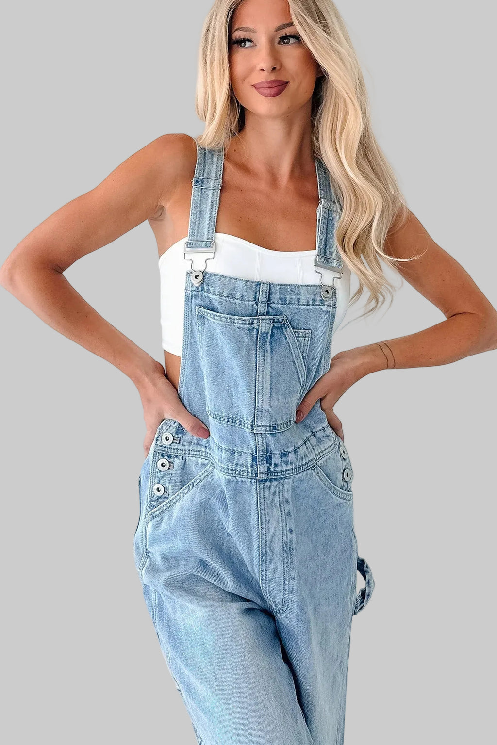 Woman wearing light blue denim overalls on a white background