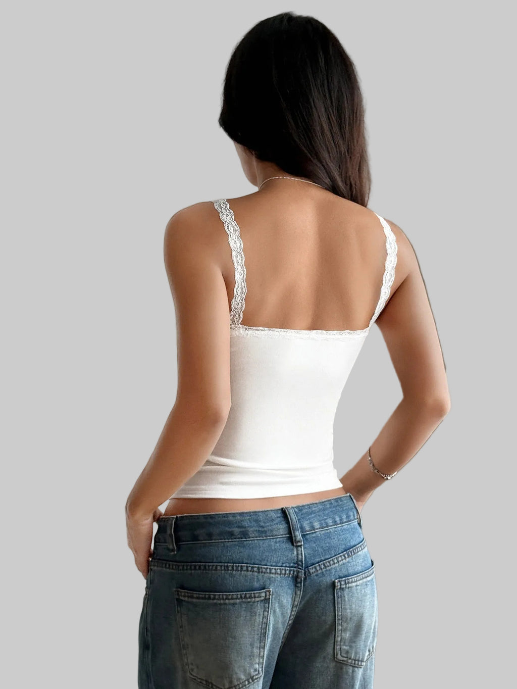 Woman wearing a white lace top and blue jeans in a bright room.