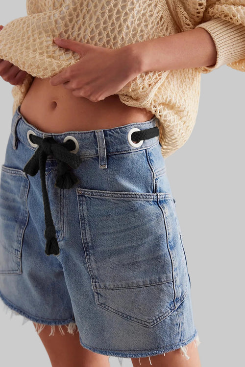 Person wearing a beige sweater and blue denim shorts with a white background
