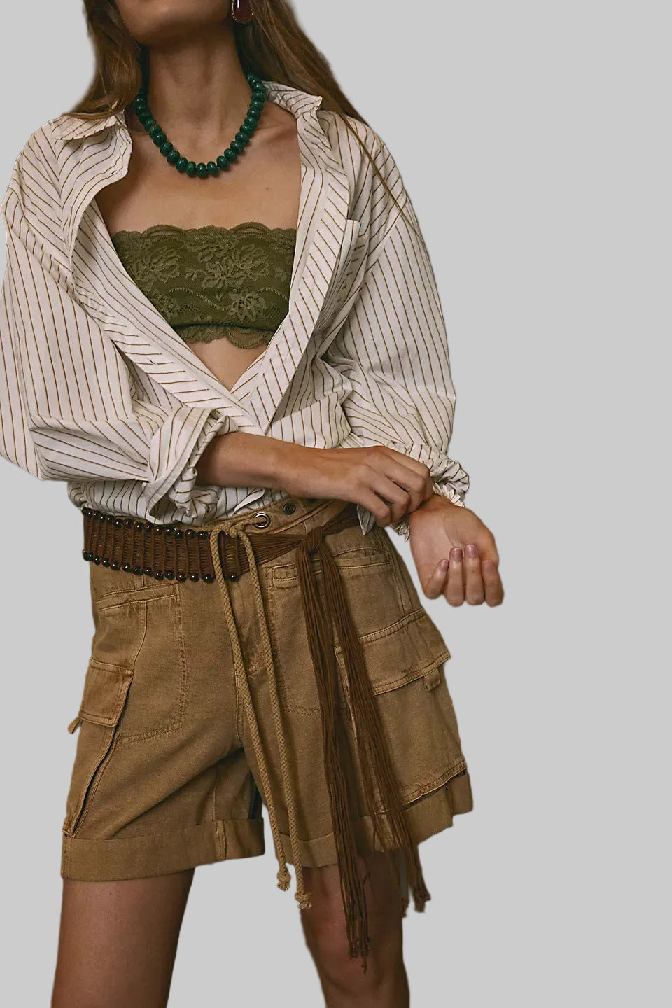 Person wearing a striped shirt, green crop top, and beige shorts with a belt against a dark background