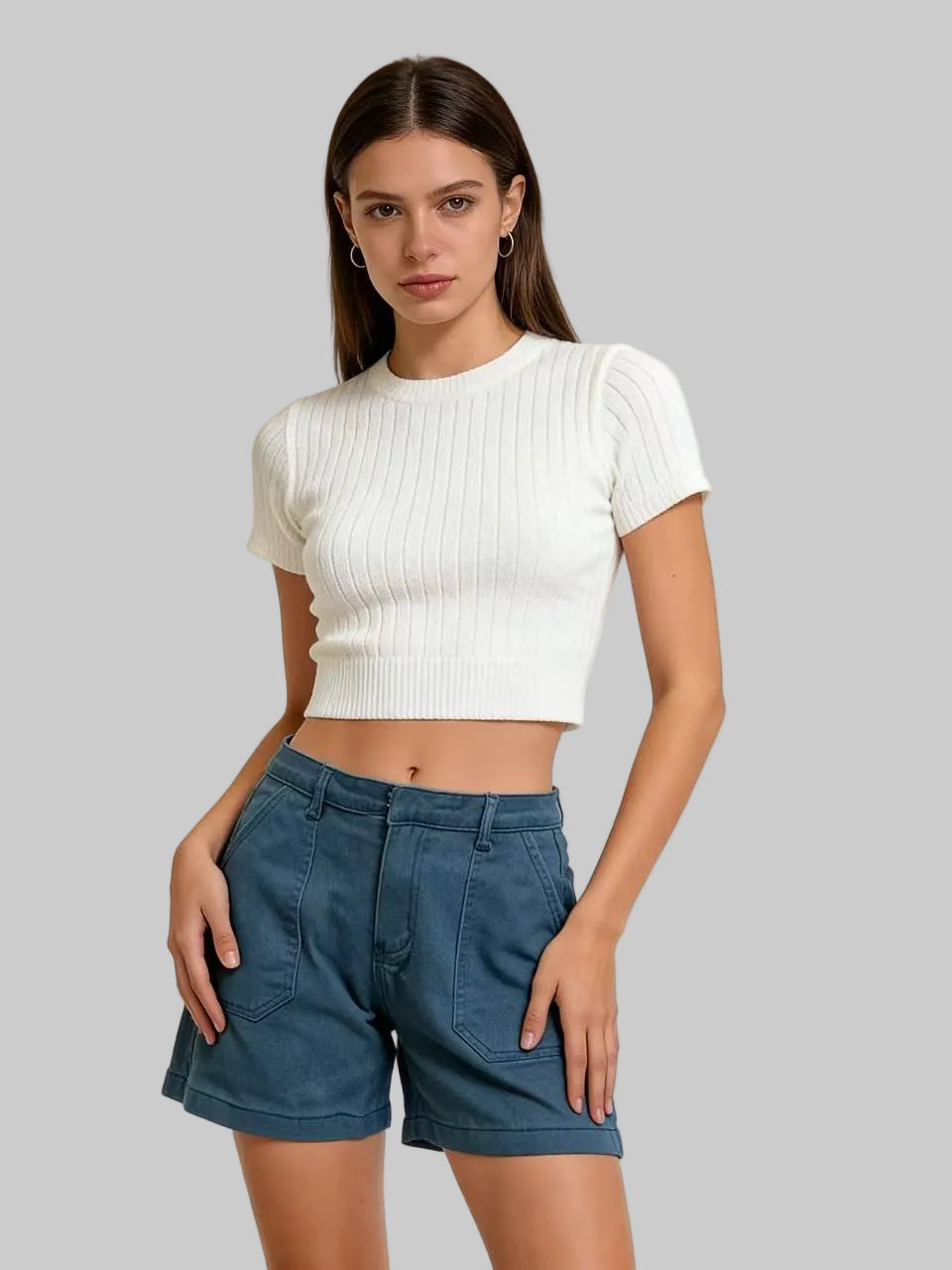 Woman wearing a white cropped top and blue shorts against a beige background