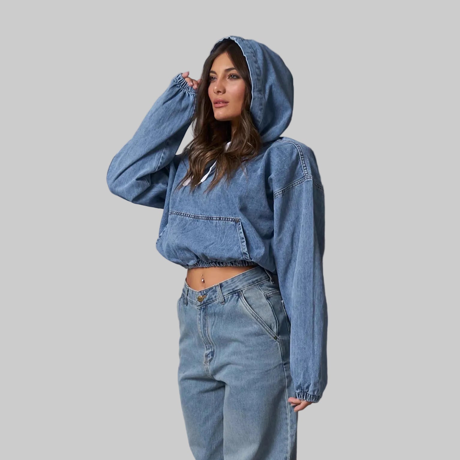 Woman wearing a blue denim hoodie and jeans against a gray background