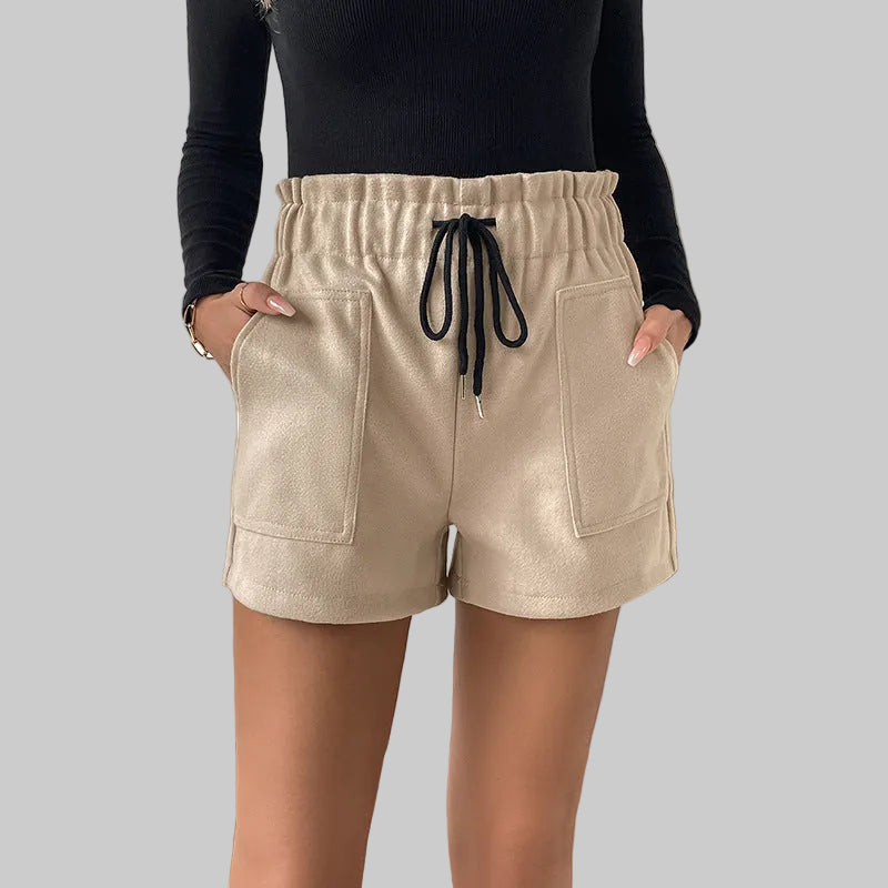 Person wearing beige shorts with a black top in a room with a plant.
