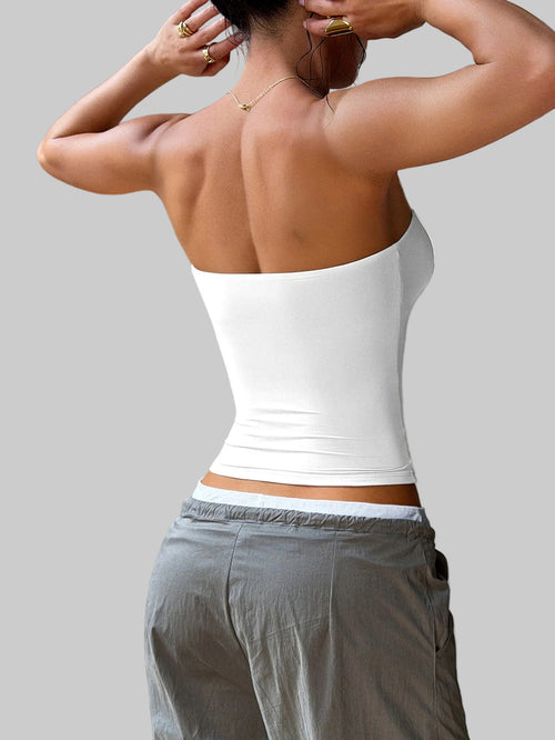 Person wearing a white tank top and gray pants against a neutral background