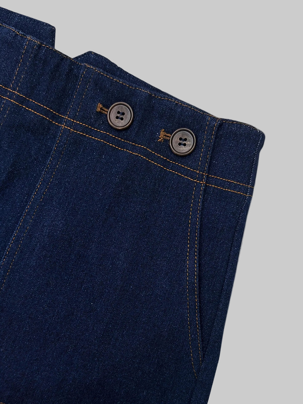 Close-up of blue denim pants with button details on a light gray background