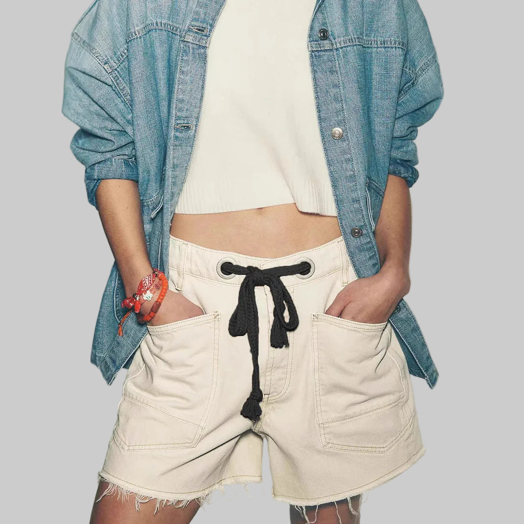 Person wearing a denim shirt over a white top and beige shorts with a black drawstring, against a plain background.