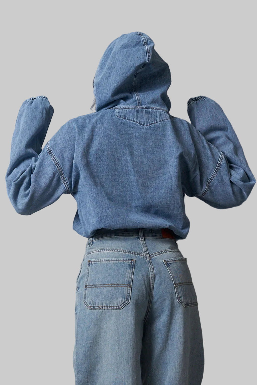 Person wearing a blue denim jacket and pants against a metallic wall.