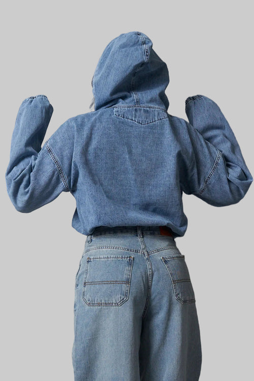 Person wearing a blue denim jacket and pants against a metallic wall.