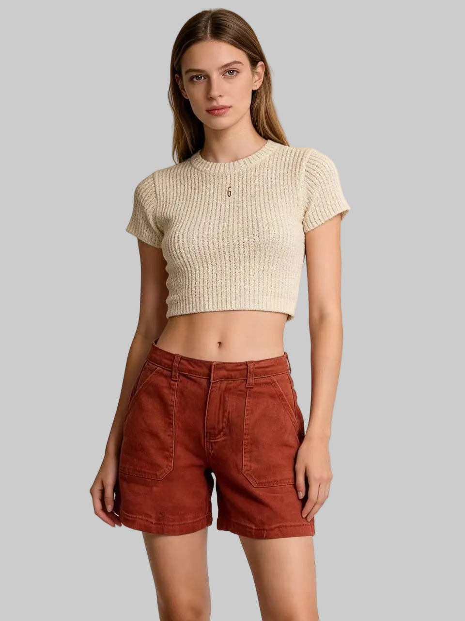 Woman wearing a beige ribbed crop top and rust-colored shorts against a beige background