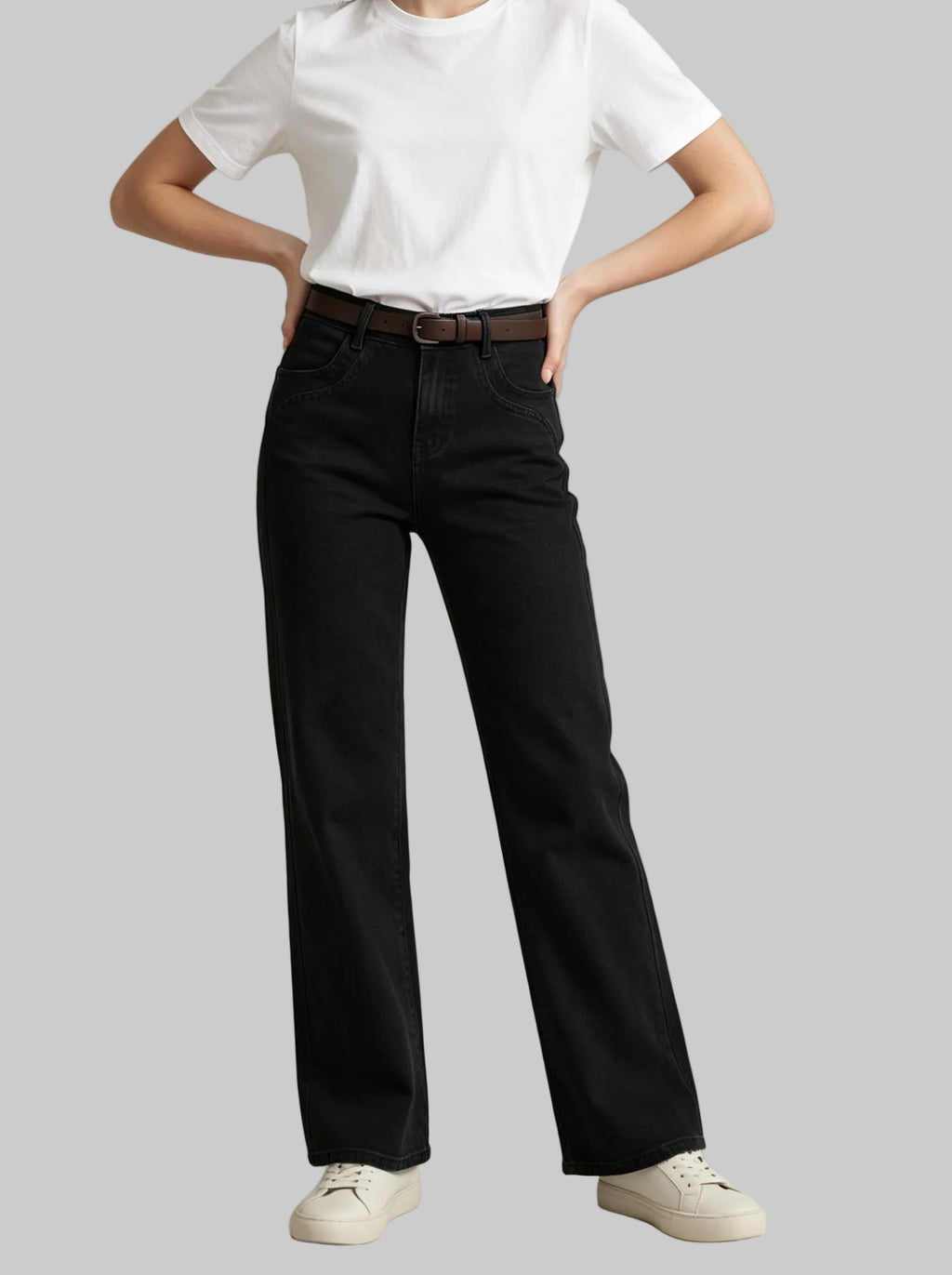 A model wearing black wide-leg jeans with a dark brown leather belt, styled with a white t-shirt and off-white sneakers, standing against a light gray studio background.