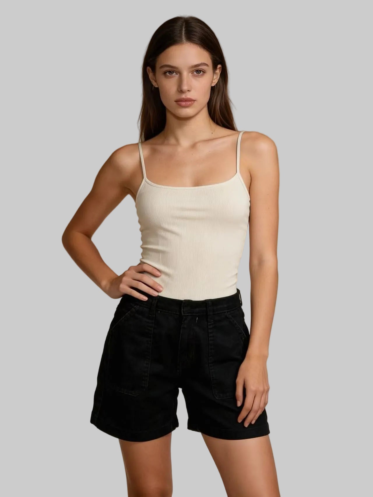 Woman wearing a white tank top and black shorts against a beige background