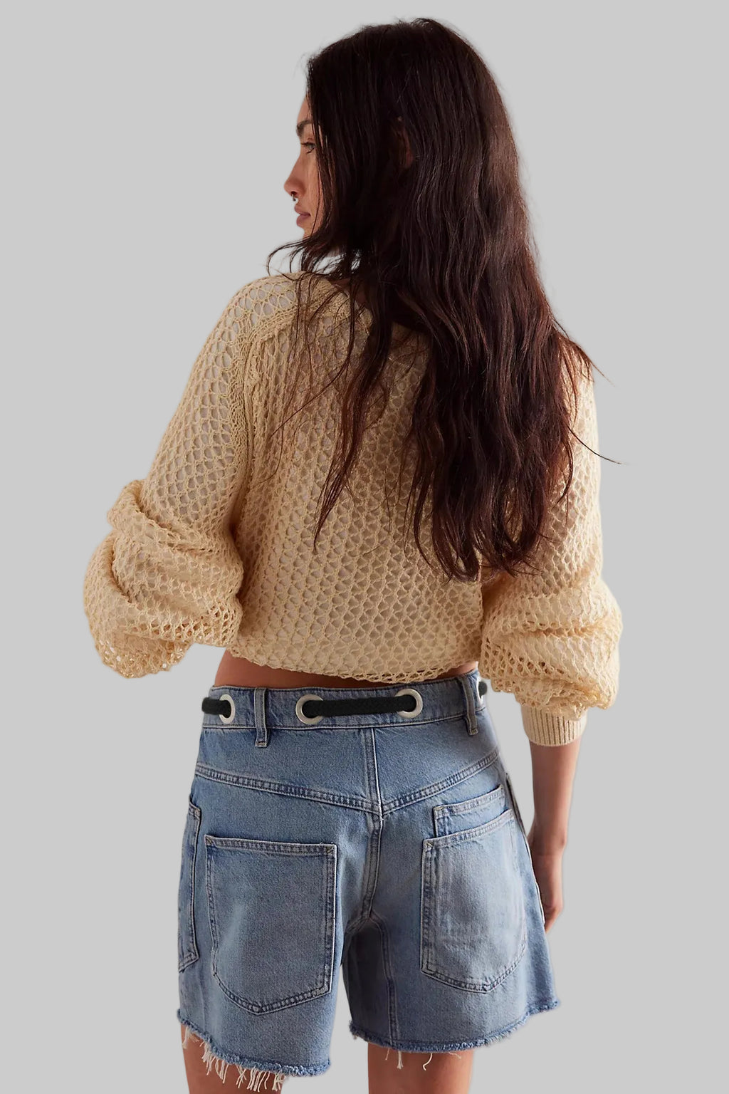 Person wearing a beige knitted sweater and denim shorts against a plain background