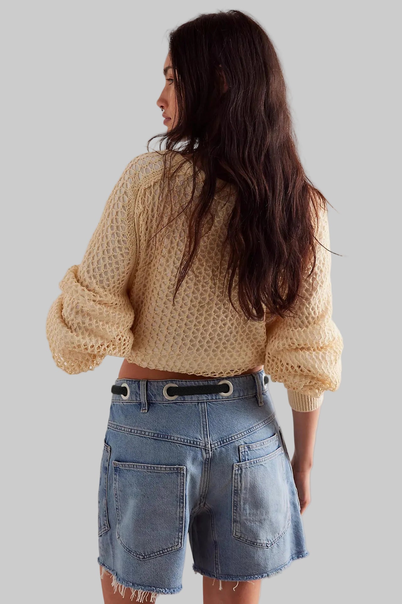 Person wearing a beige knitted sweater and denim shorts against a plain background