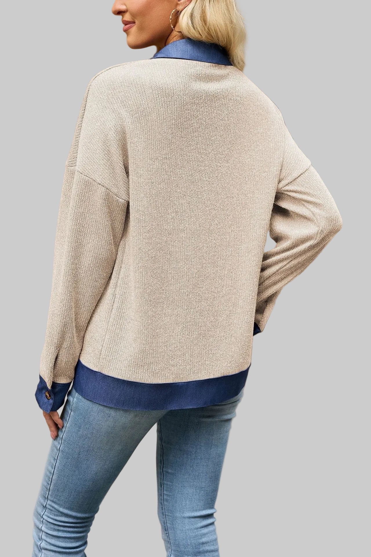 A woman wearing a beige knit cardigan with blue ribbed trim, shown from the back in an outdoor urban setting.