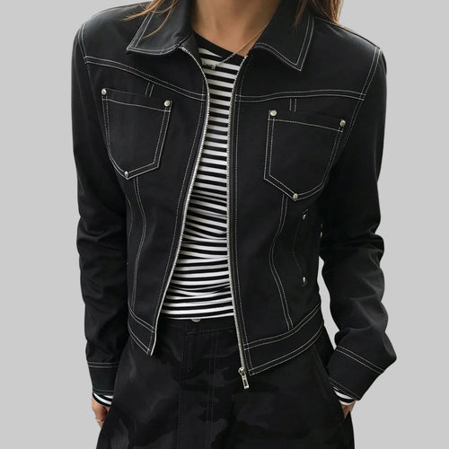 A person wearing a black cropped denim jacket with white contrast stitching, silver snap details, and a front zipper, layered over a black and white striped shirt.