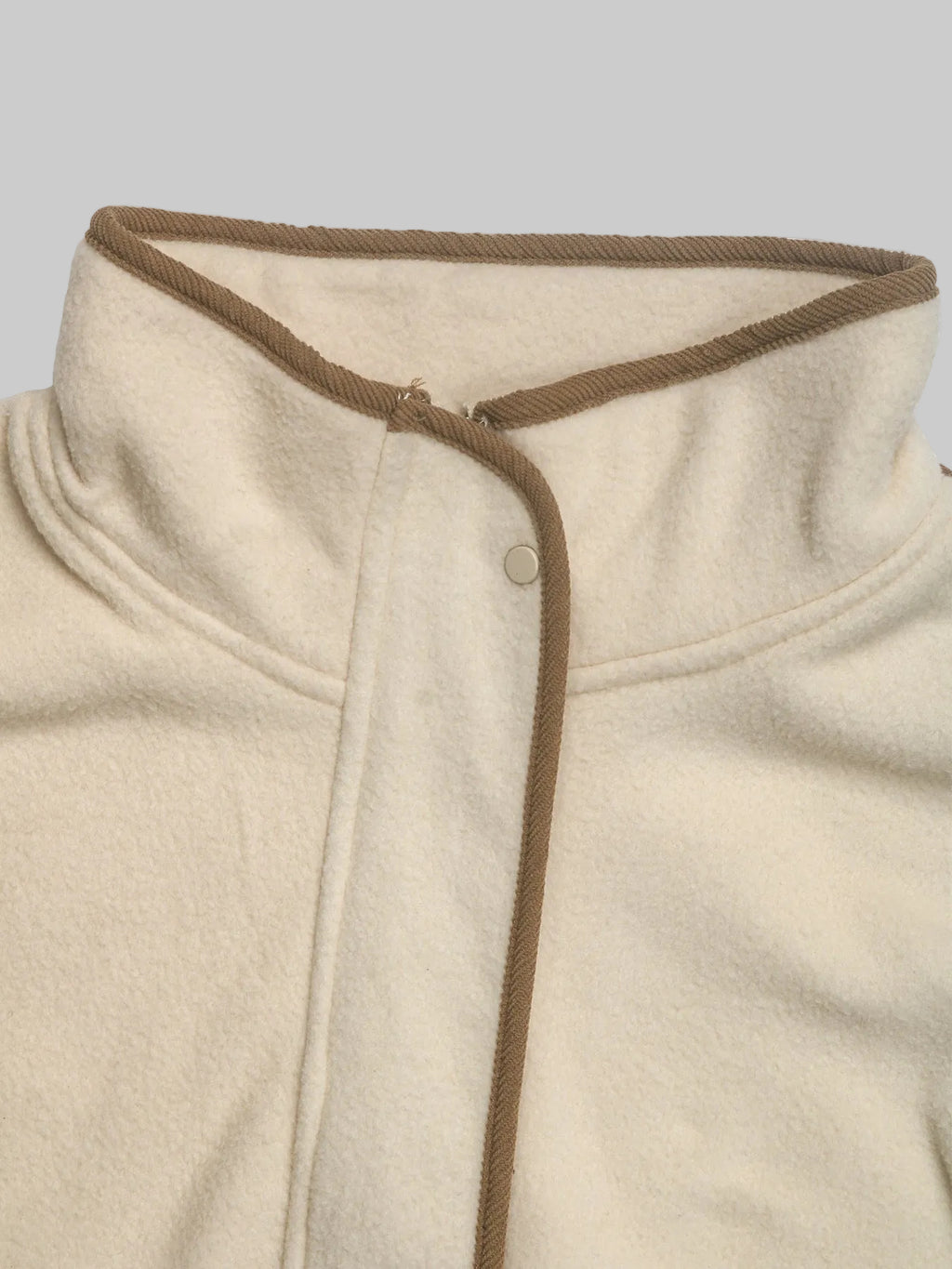 Close-up of a cream-colored fleece jacket with a brown braided trim along the collar and front placket.