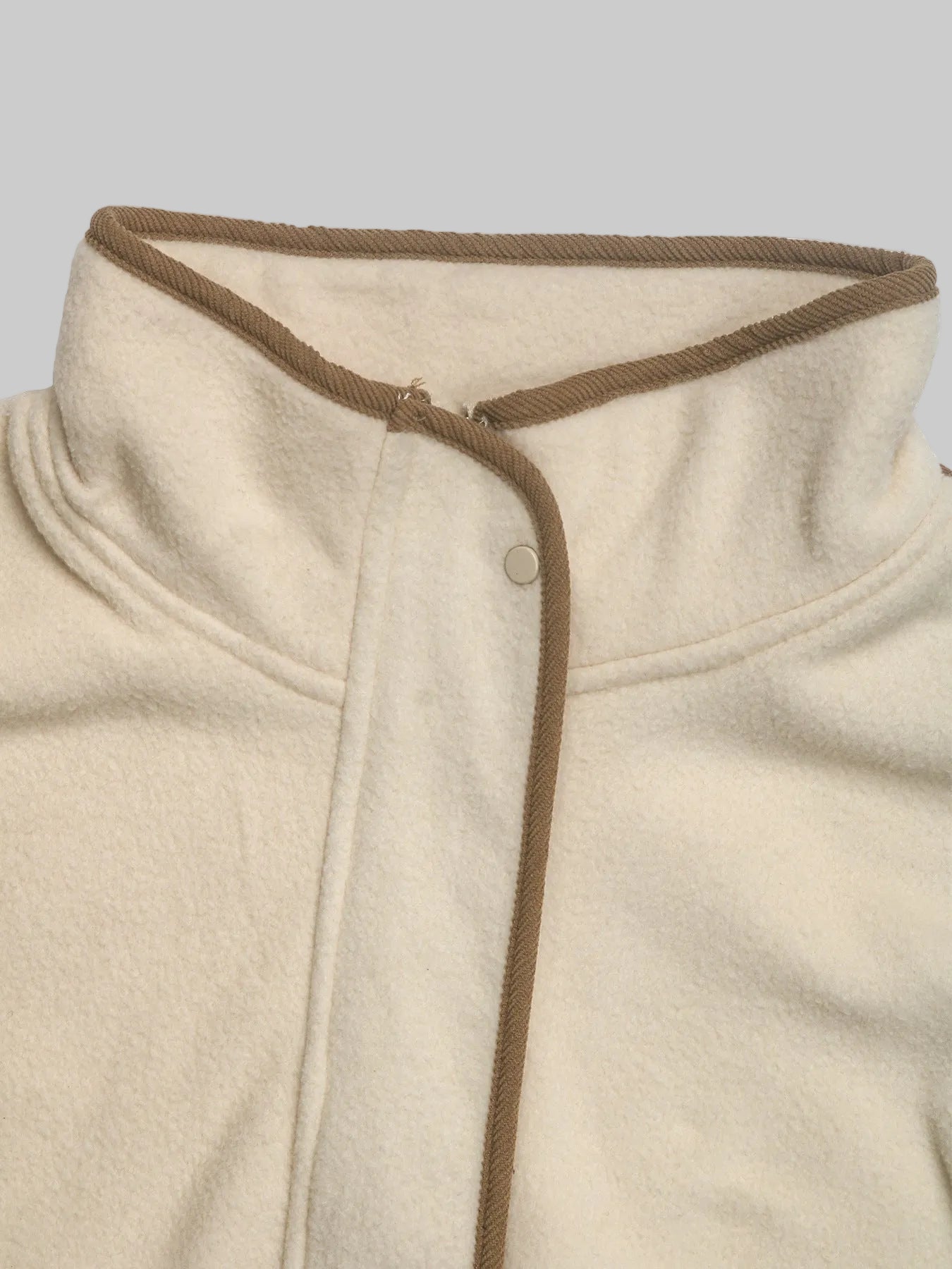 Close-up of a cream-colored fleece jacket with a brown braided trim along the collar and front placket.