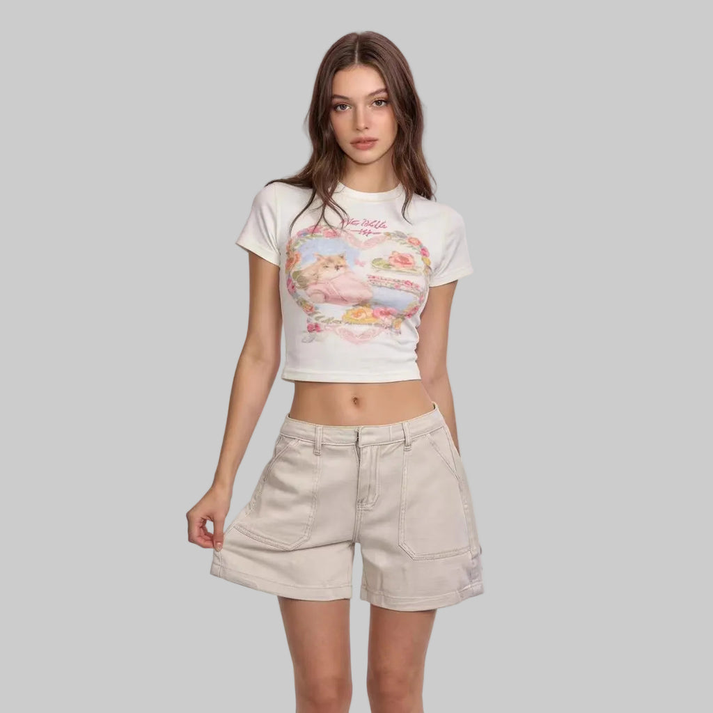Woman wearing a white t-shirt with a graphic design and beige shorts on a light pink background