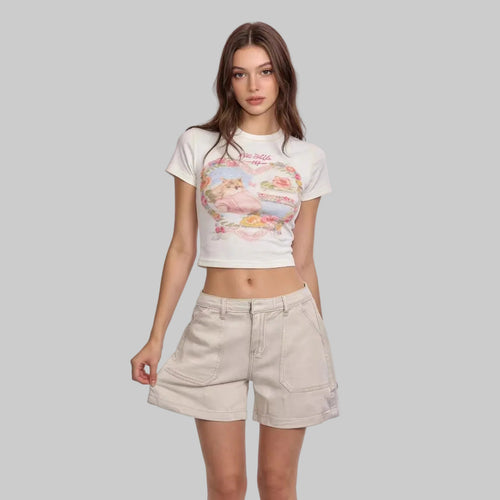 Woman wearing a white t-shirt with a graphic design and beige shorts on a light pink background