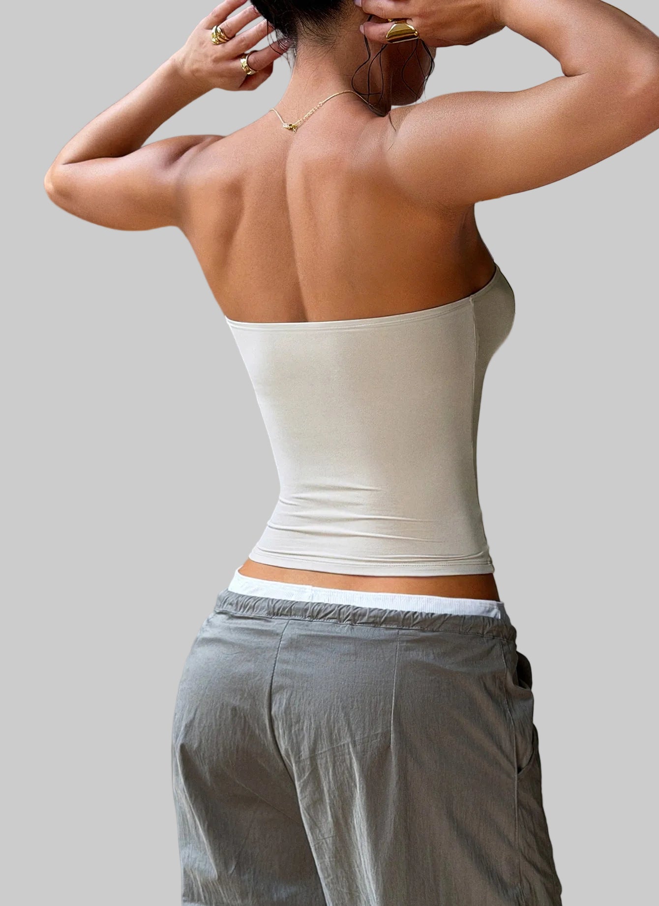 Person wearing a beige strapless top and gray pants against a neutral background
