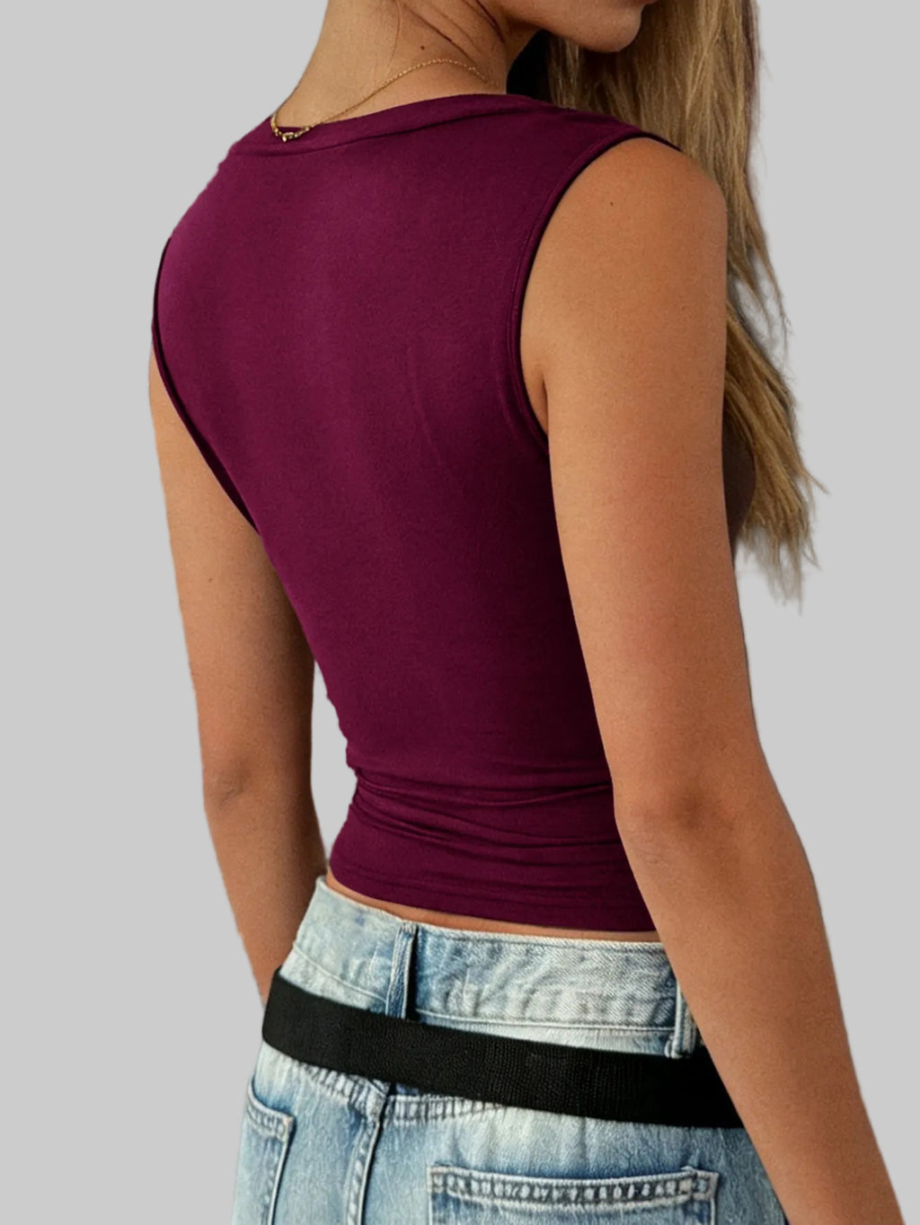 Person wearing a maroon tank top and blue jeans against a stone wall.