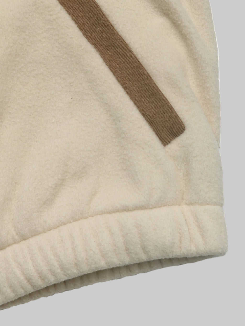 Close-up of a cream-colored fleece garment with a ribbed cuff and a diagonal brown stripe detail, shown against a white background.