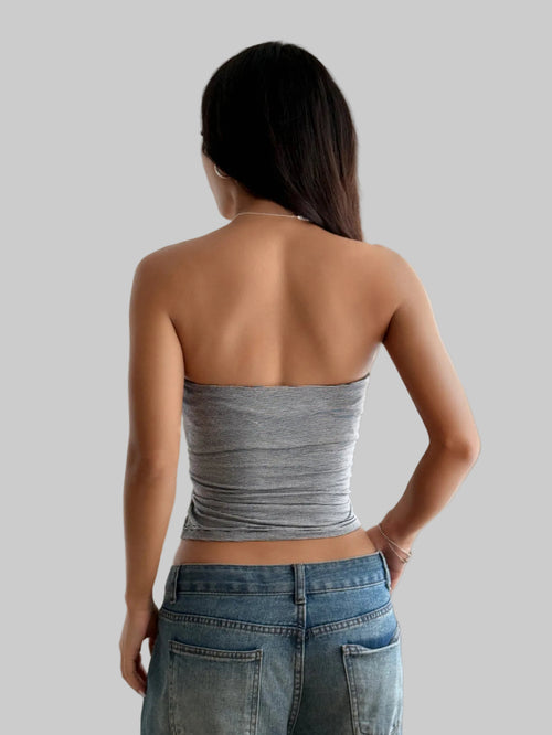 Woman wearing a strapless gray top and blue jeans in a bright room.