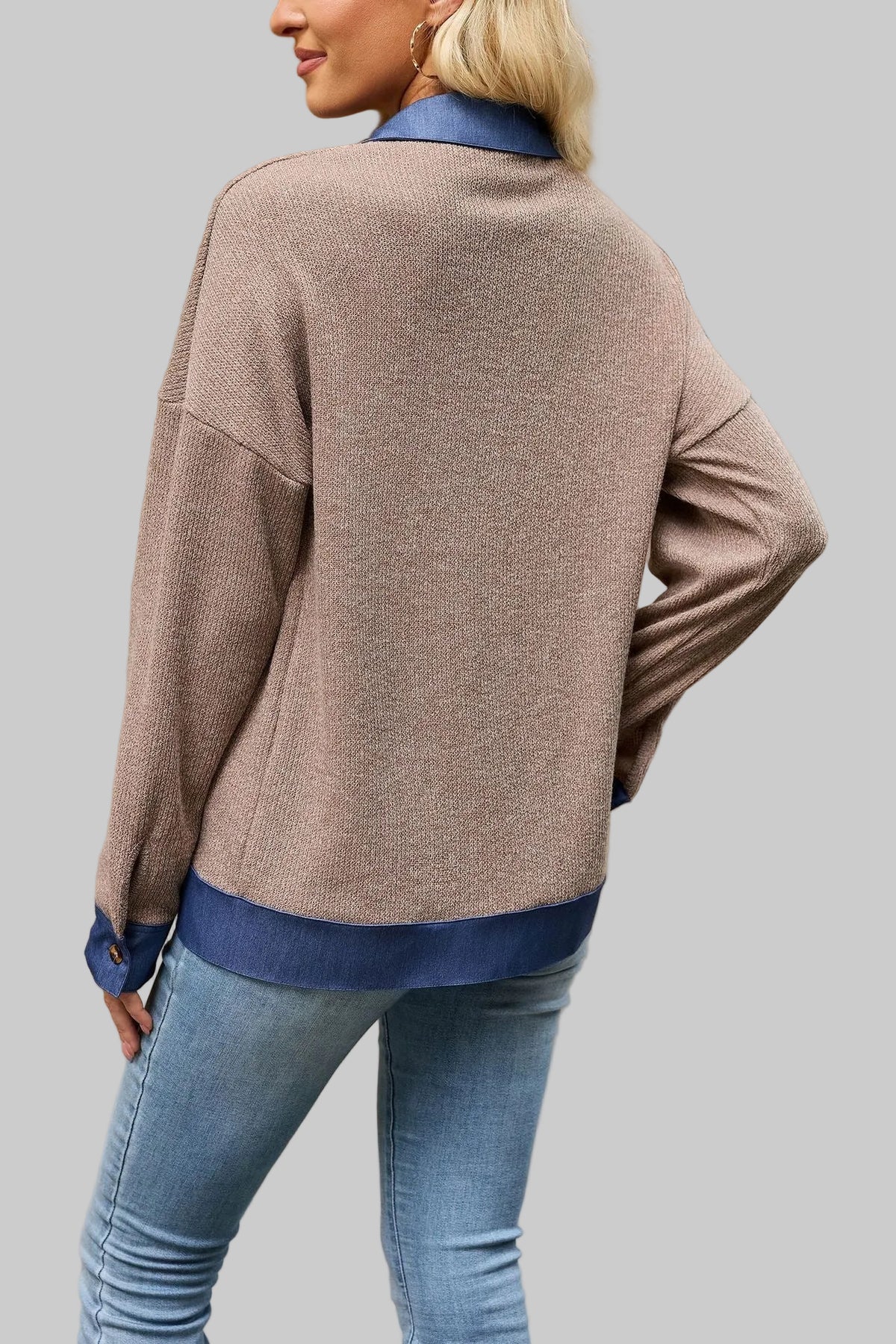 A woman wearing a taupe knit cardigan with blue ribbed trim, shown from the back in an outdoor urban setting.