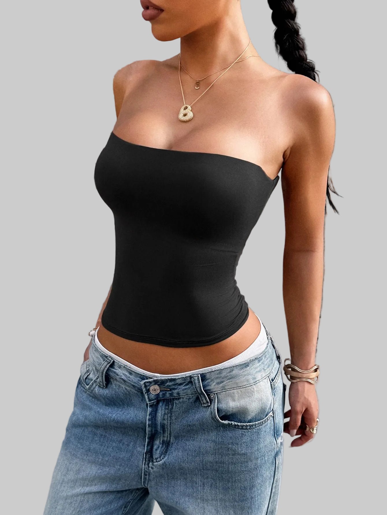 Person wearing a black strapless top and blue jeans against a concrete wall.