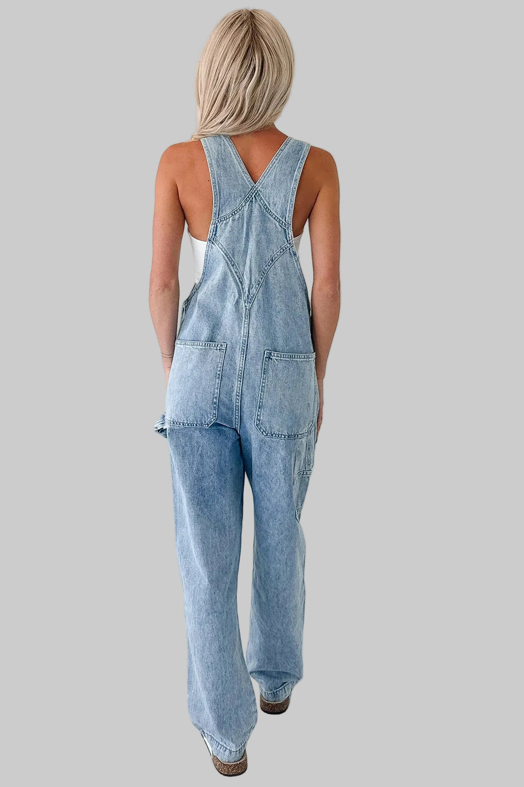 Person wearing light blue denim overalls on a white background