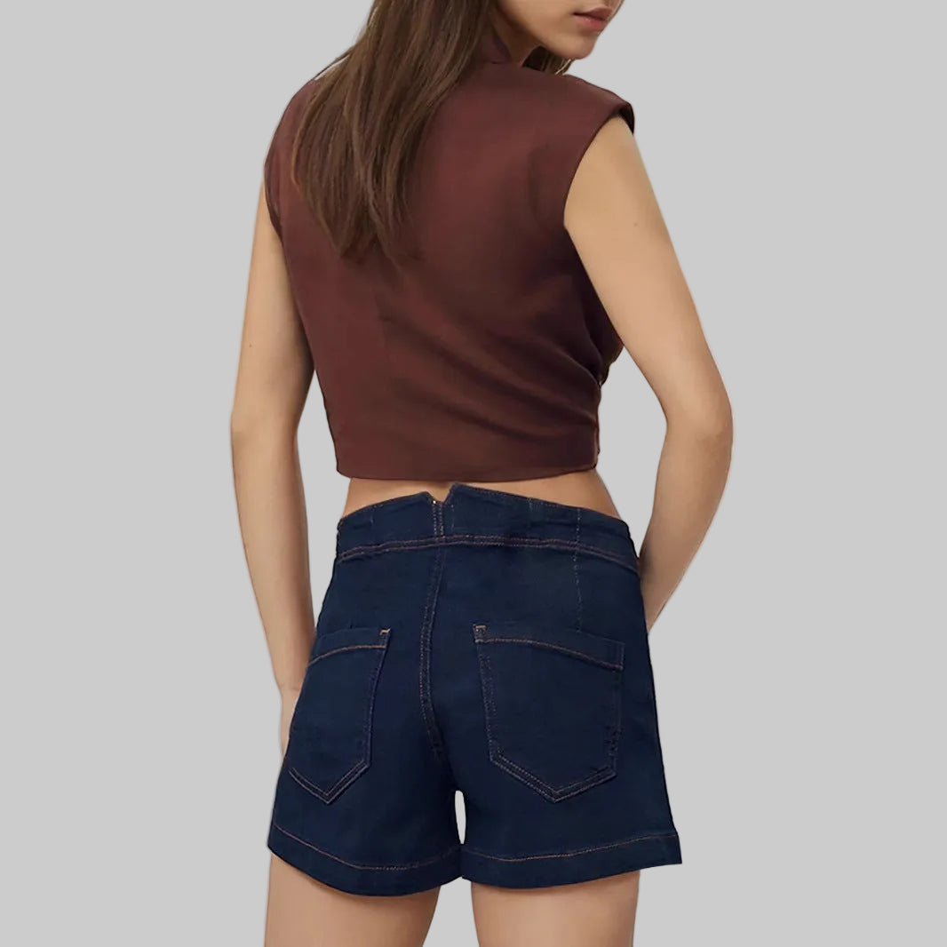 Person wearing a brown sleeveless top and dark blue denim shorts on a light gray background